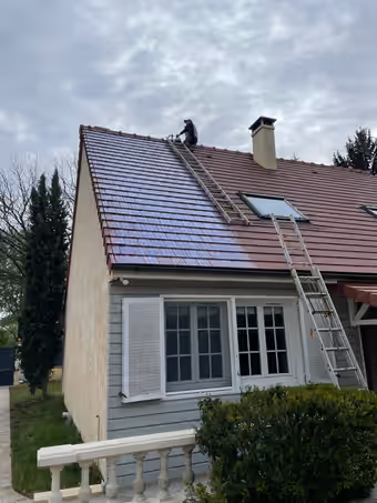 Couvreur au faîtage d’un pavillon, un pan de tuiles traité et brillant, l’autre encore mat